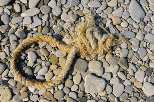 Preview: Old Worn Battered Marine Rope On The Pebble Beach On A Sunny Summer Day, Top View