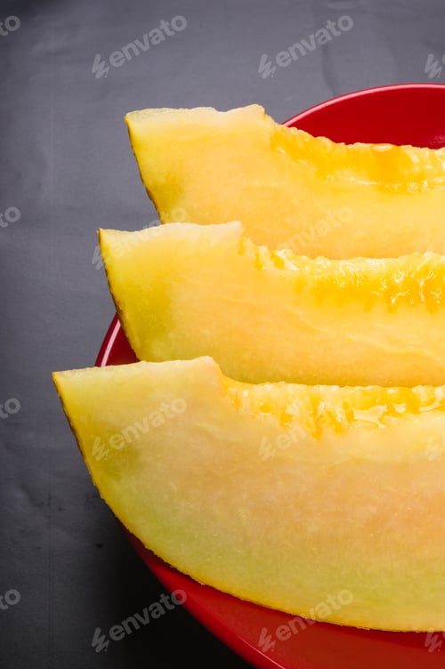 Preview: Slices Of Ripe Juicy Melon In Red Plate On Black Background