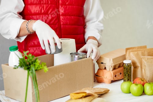 Preview: Volunteer In The Protective Medical Mask And Gloves Putting Food In Donation Box. Delivery Man