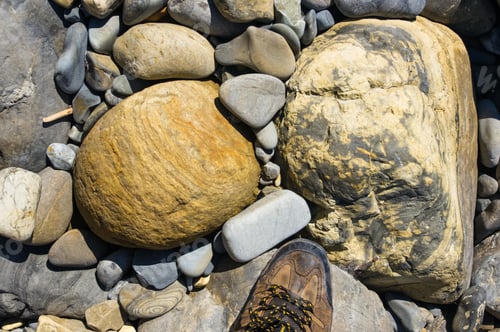 Preview: Hiking Boots, Boulders And Colorful Pebbles On The Beach On A Warm Summer Day