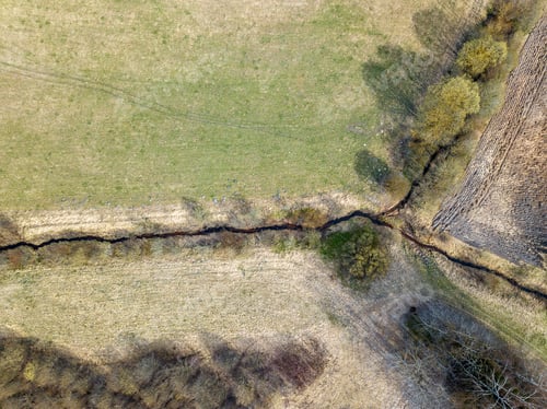 Preview: Aerial View Of Small Country River Bed Wavy In Spring Time In Countryside With Dry Grass And Some