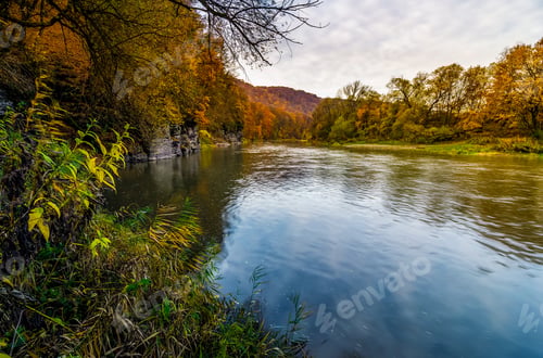 Preview: Forest River In Autumn Mountains. Lovely Grassy Shores With Yellowed Trees And Rocky Cliff