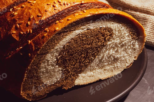 Preview: Unusual Two-Color Fresh Loaf Of Bread In A Ceramic Plate And A Woven Napkin On A Black Background