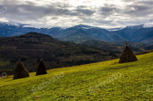 Preview: Haystack On The Rural Field On Hillside. Gorgeous Countryside With Snowy Mountain Ridge In The