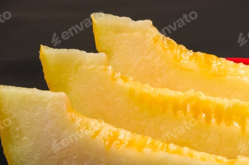 Preview: Slices Of Ripe Juicy Melon In Red Plate On Black Background