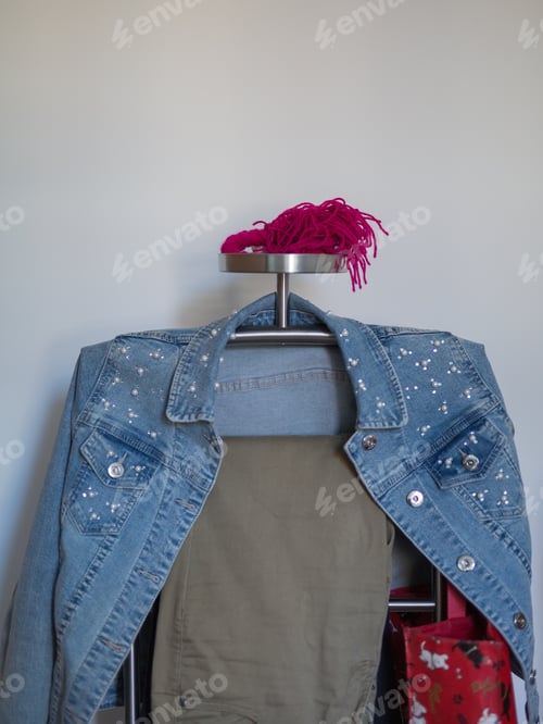 Preview: Jeans Jacket With White Beads And Beige Trousers Hanging On A Metal Coat Rack.