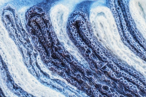 Vorschau: Weißer und grauer Strickstoff aus nächster Nähe. Textur aus gestricktem Stoff für Winterkleidung.