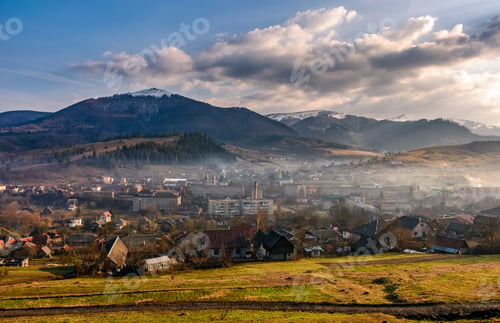 Preview: Rural Area In Mountains With Snowy Peaks. Agricultural Field In Fog On A Hillside Near The Village
