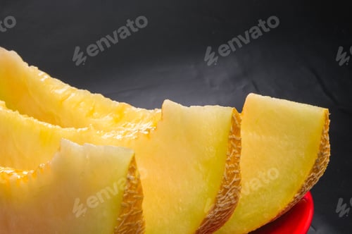 Preview: Slices Of Ripe Juicy Melon In Red Plate On Black Background
