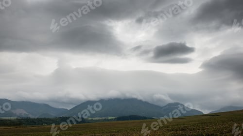 Preview: Dark Storm Clouds Over Meadow With Green Grass And Mountains In Background
