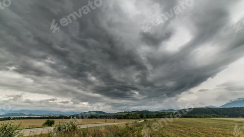 Preview: Dark Storm Clouds Over Meadow With Green Grass And Mountains In Background