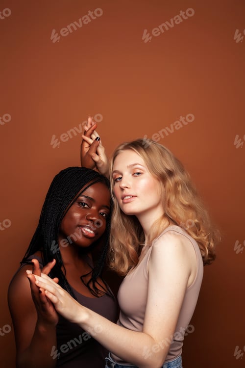 Preview: Two Pretty Girls African And Caucasian Blond Posing Cheerful Together On Brown Background