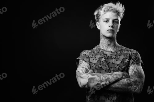 Preview: Studio Shot Of Young Handsome Rebellious Man With Blond Hair And Tattoos Against Black Background