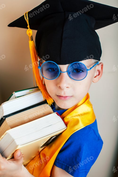 Preview: Little Cute Preschooler Boy In Glasses With Books At Home Education In Graduate Hat Smiling Posing