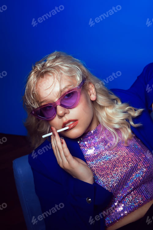 Preview: Woman In The Style Of The 70S, 80S, 90S. A Blonde Woman In Bright Glasses And With A Cigarette Sits