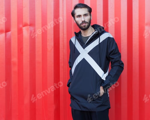 Vista previa: A Bearded Hipster In A New Trendy Black Windbreaker On A Red Background Posing On A Summer Evening