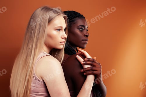 Preview: Two Pretty Girls African And Caucasian Blond Posing Cheerful Together On Brown Background