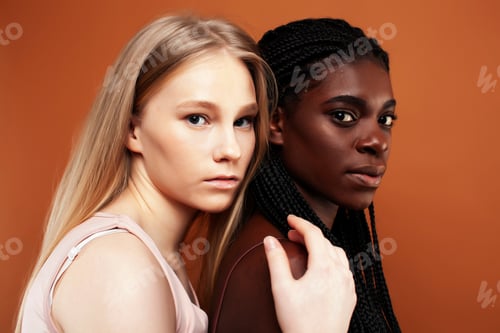 Preview: Two Pretty Girls African And Caucasian Blond Posing Cheerful Together On Brown Background
