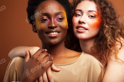 Preview: Two Pretty Girls African And Caucasian Blond Posing Cheerful Together On Brown Background