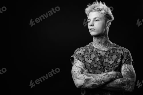 Preview: Studio Shot Of Young Handsome Rebellious Man With Blond Hair And Tattoos Against Black Background