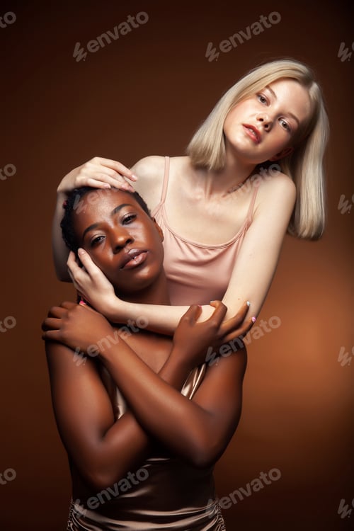 Preview: Two Pretty Girls African And Caucasian Blond Posing Cheerful Together On Brown Background
