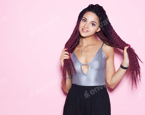 Preview: Beautiful Young Girl Playing With Her Braids In A Fashionable Outfit. Portrait In Studio On A Pink