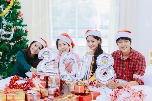 Visualização: Grupo de jovens alegres em chapéus de Papai Noel comemorando o Ano Novo junto com balões