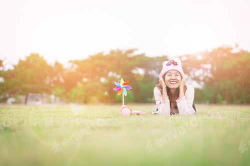 Preview: Beautiful Girl With Wind Toy Or Wind Turbine Or Pinwheel And Wool Hat Sitting On Meadow In Winter