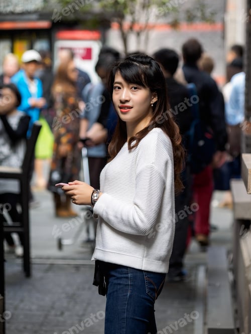 Preview: Front View Of A Happy Chinese Girl Walking And Using A Smart Phone In Crowded Street.