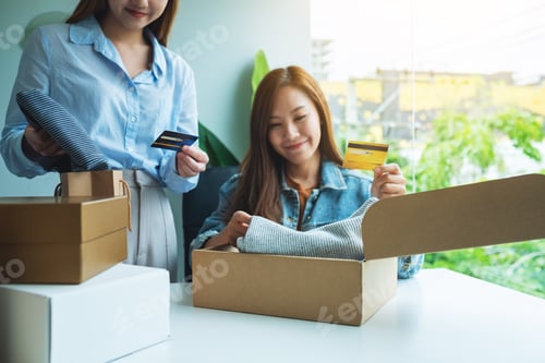 Preview: Two Women Holding And Using Credit Card For Online Shopping While Opening A Postal Parcel Box Of