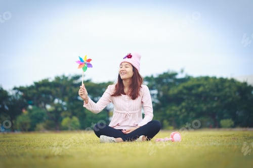 Visualização: Linda garota segurando brinquedo eólico ou turbina eólica ou cata-vento e chapéu de lã sentada no prado
