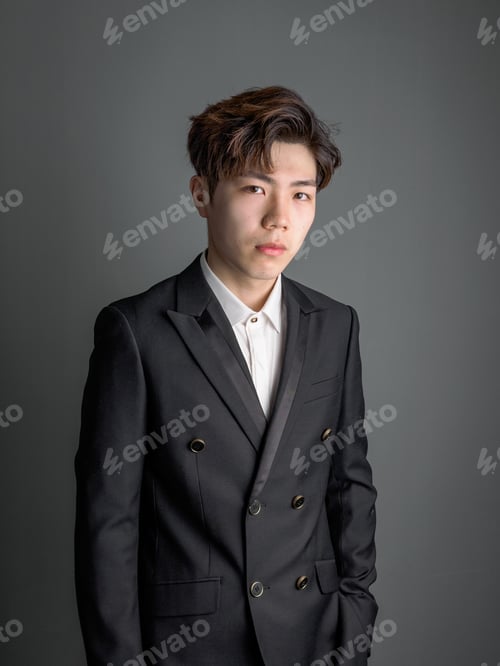 Preview: Portrait Of A Smart Young Chinese Man Standing Against Gray Background, Looking At Camera With