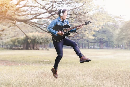 Preview: Asian Young Men Jump In Nature Playing Guitar And Listen To Music With Headphones.