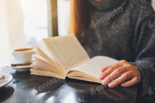 Preview: Closeup Image Of A Beautiful Woman Holding And Reading A Book With Coffee Cup On The Table
