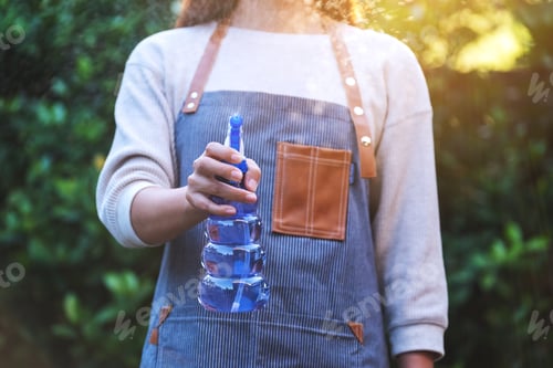 Preview: A Woman With Apron Watering Plant By Foggy Spray In Garden