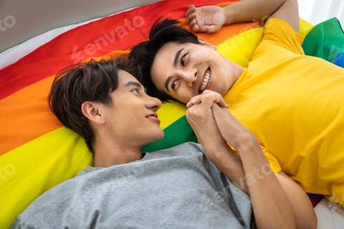 Preview: Happy Asian Homosexual Gay Couple Lying On Rainbow Pride Flag, Holding Hand. Lgbt Concept.