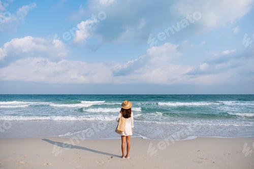 Preview: Rear View Image Of A Woman With Hat And Bag Strolling On The Beach With Blue Sky Background