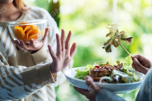Preview: Women Choosing To Eat Potato Chips And Making Hand Sign To Refuse A Vegetables Salad