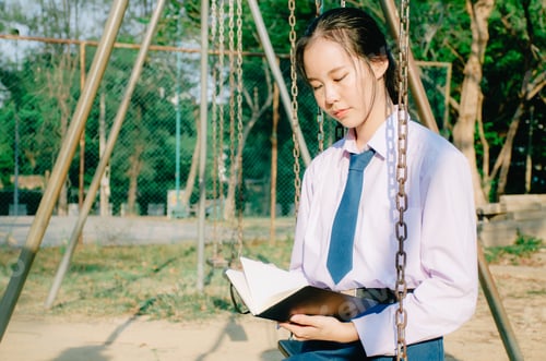 Preview: Lovely Teenage Girl Wearing School Uniform Reading Book While Sitting On A Swing At The Park
