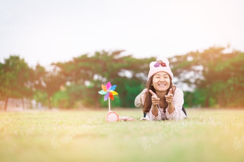 Preview: Beautiful Girl With Wind Toy Or Wind Turbine Or Pinwheel And Wool Hat Sitting On Meadow In Winter