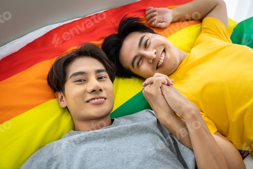 Preview: Happy Asian Homosexual Gay Couple Lying On Rainbow Pride Flag, Holding Hand. Lgbt Concept. Looking