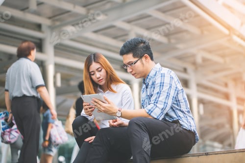 Preview: Young Businessman And Businesswoman Using Digital Tablet With Colleagues In Background At Walkway