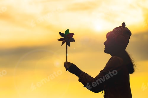 Preview: Silhouette Of Beautiful Girl Holding Wind Toy Or Wind Turbine Or Pinwheel And Wool Hat At Meadow On