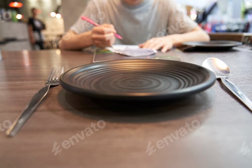 Preview: Close-Up Image Of Plate And Spoon, The Backdrop Is A Picture Of People Ordering Food.