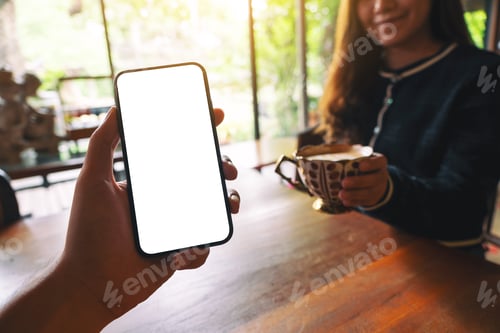 Preview: Mockup Image Of A Man'S Hand Holding Black Mobile Phone With Blank White Screen With Woman Drinking