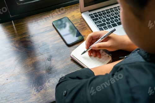 Preview: Woman Writing Daily Notebook Next To Cellphone And Laptop