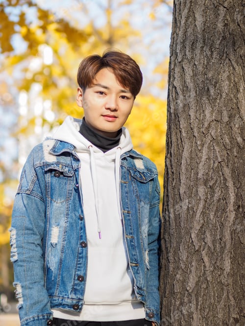 Preview: Young Chinese Smiling Man Portrait Stand With Blur Yellow Trees Background In Sunset In Autumn