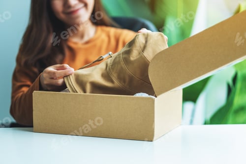 Preview: A Woman Receiving And Opening A Postal Parcel Box Of Clothing At Home For Delivery And Online