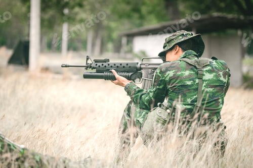 Preview: Soldier Sitting On The Ground And Camouflage In Grass. Soldier Holding Gun Weapon And Waring Armor