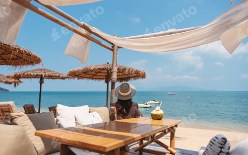 Vista previa: Rear View Image Of A Woman Looking At A Beautiful Sea While Sitting In The Cafe On The Beach
